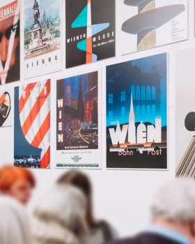 Mehrere bunte historische Werbeplakate sind in einem Archiv auf Schiebewänden aus Metall präsentiert, darunter ein Retro-Plakat mit einer Frau und der Aufschrift „so gut – Manner Neapolitaner“.