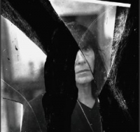 Friederike Mayröcker. Foto: Marko Lipuš Schwarz-Weiß-Photographie: Portrait einer dunkelhaarigen Frau, die sich in Spiegelscherben spiegelt