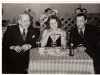 Schwarz-Weiß-Foto: Frau und zwei Männer an gedecktem Tisch mit kariertem Tischtuch sitzend