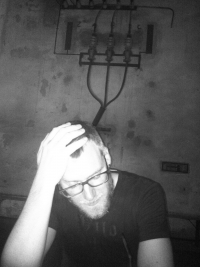 Patrick Pulsinger Schwarz-Weiß-Photographie: junger Mann mit Brille und Bart stützt Kopf auf Hand